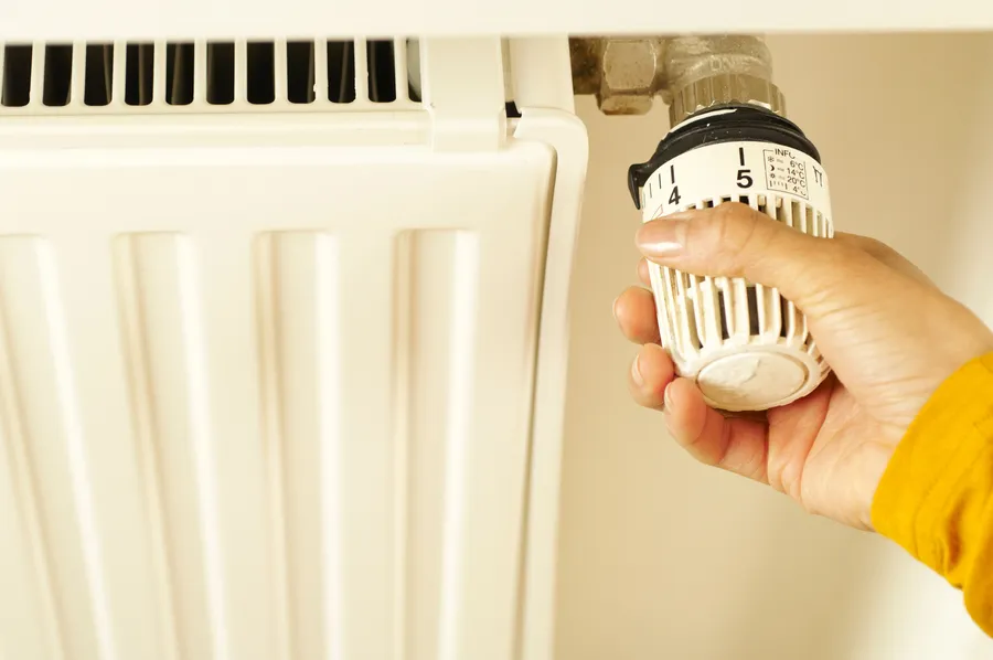 Hand stellt einen Heizkörper-Thermostat ein